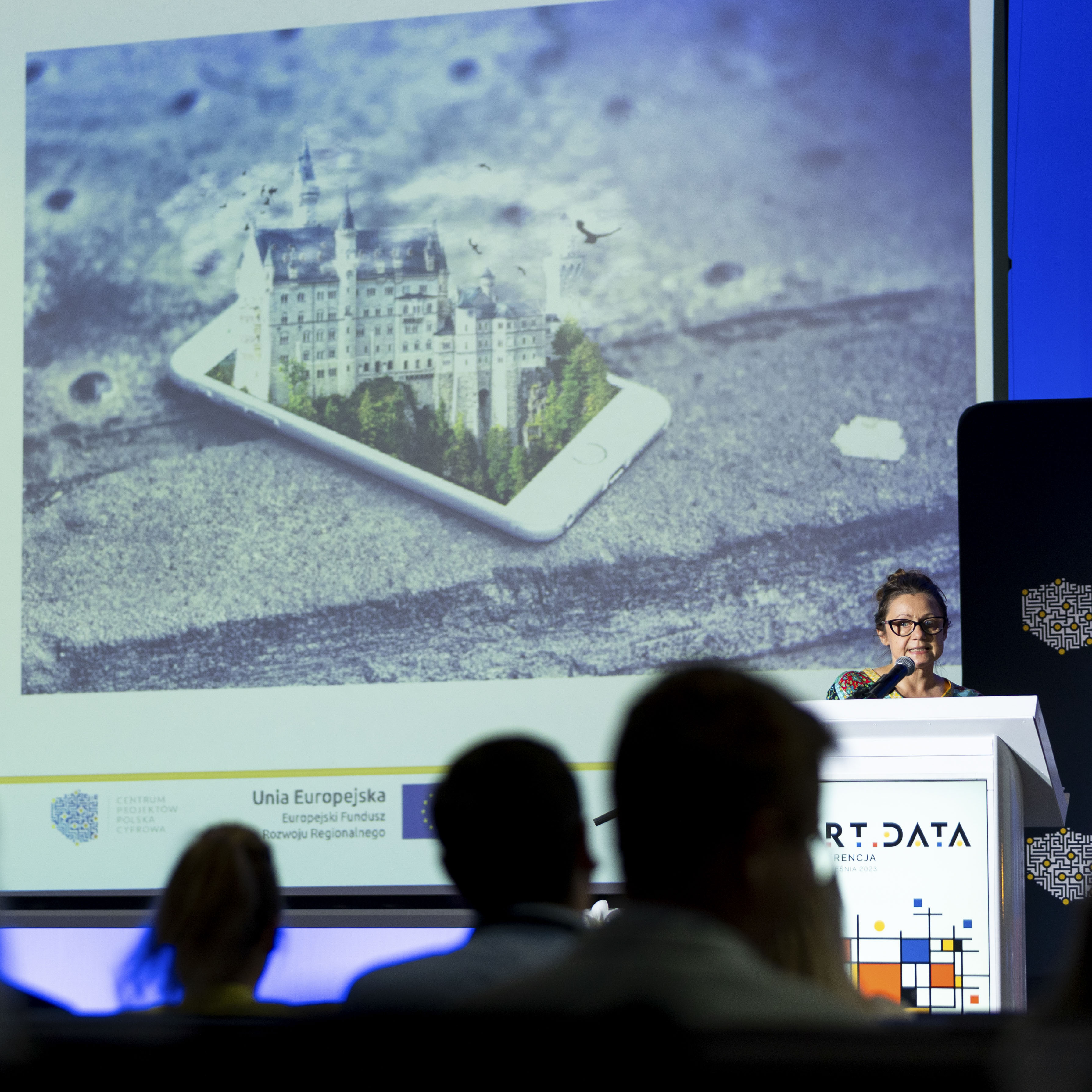 Pani Anna Osiadacz Prezeska Fundacji Koncept Kultura w trakcie prezentacji pod tytułem „Wykorzystanie danych w Virtual Reality”, w tle slajd przedstawiający wyłaniający się ze smartfona zamek