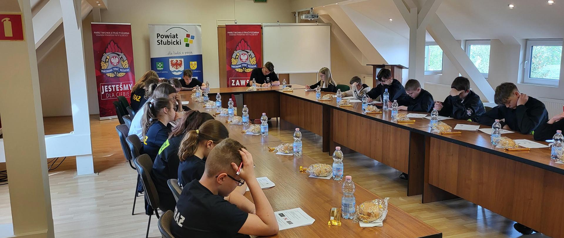 Widok wnętrza sali konferencyjnej Starostwa Powiatowego w Słubicach. Przy stolikach siedzą uczestnicy turnieju rozwiązując zadania testowe.