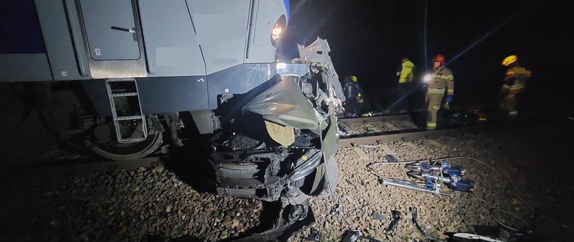 na zdjęciu widoczne miejsce wypadku uszkodzona lokomotywę i pojazd w tle strażacy