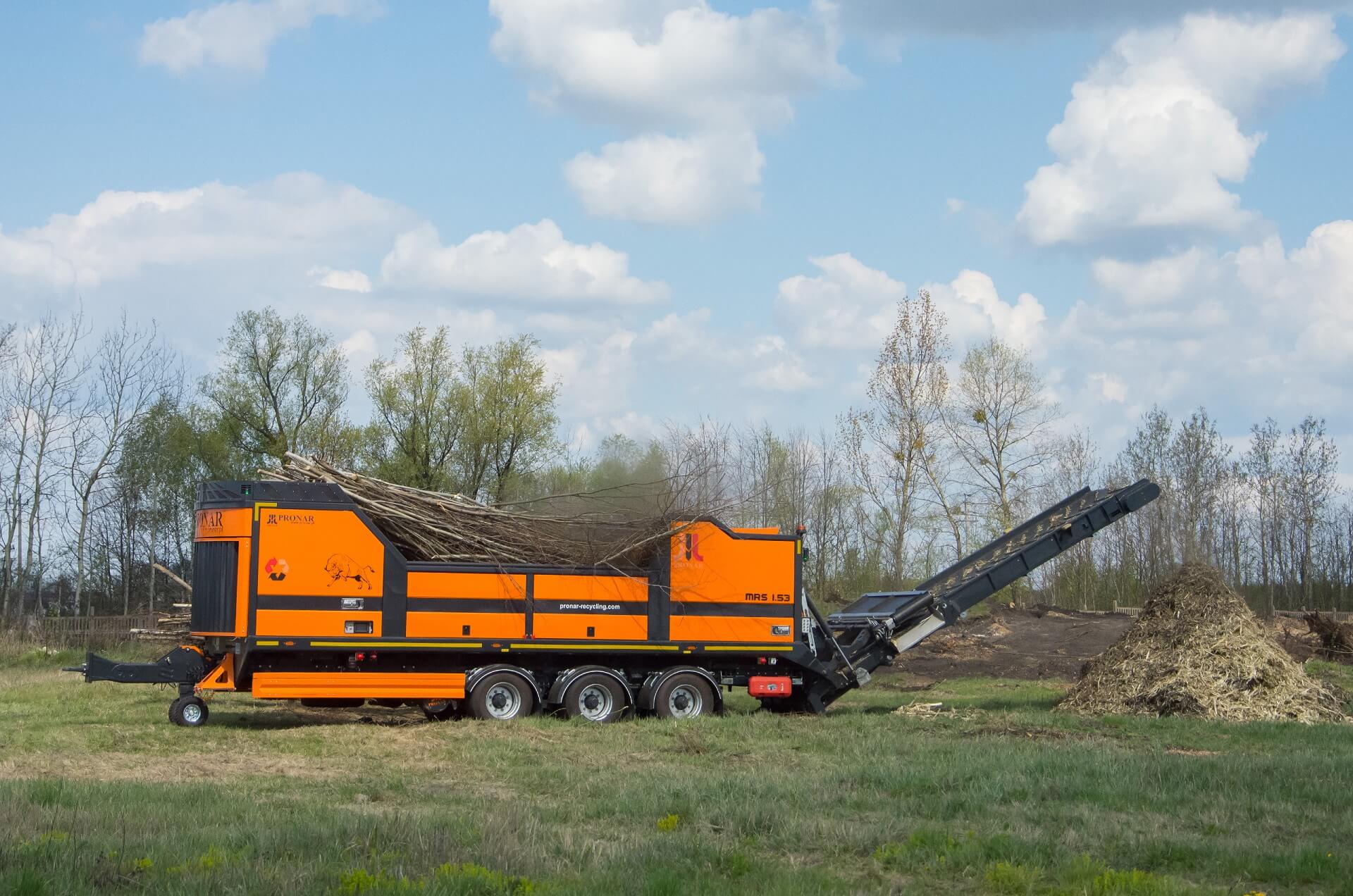 Mobile High-Speed ​​Shredder MRS 1.53. An orange machine the size of a combine harvester works in the field, mulching cut tree branches