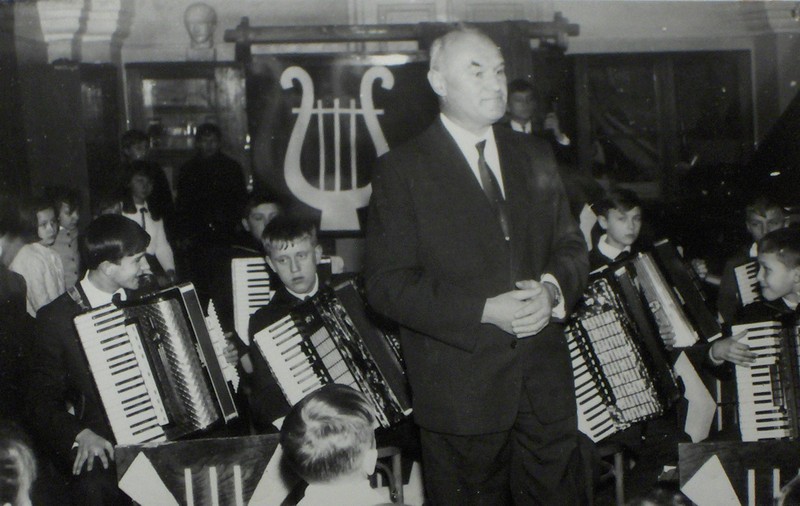 Czarno-białe zdjęcie przedstawiające uczniów zespołu akordeonowego z instrumentami. Na pierwszym planie stoi dyrektor Tadeusz Bryk. 