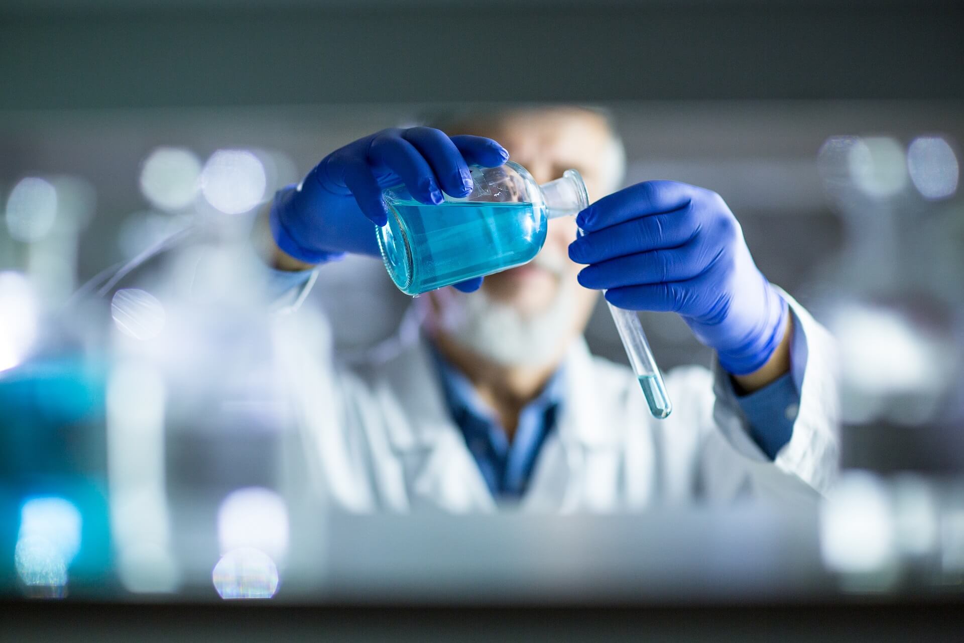 Laboratory. The man in blue gloves pours blue liquid into a test tube