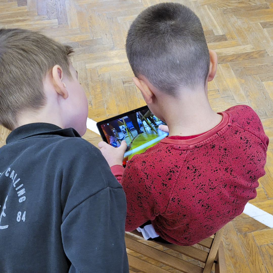 Na zdjęciu znajdują się dzieci sterujące robotem z tableta.