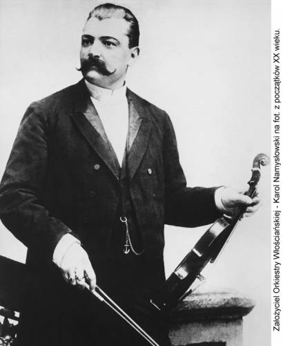 Fotografia - Karol Namysłowski stoi patrząc w prawą stronę, w lewej ręce trzyma skrzypce oparte o biodro a w prawej ręce trzyma smyczek