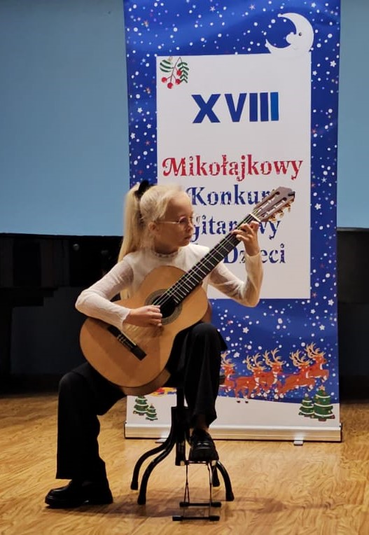 Zdjęcie Zuzanna Stach Rybik 2024 - uczennica grająca na gitarze, w tle baner reklamowy konkursu