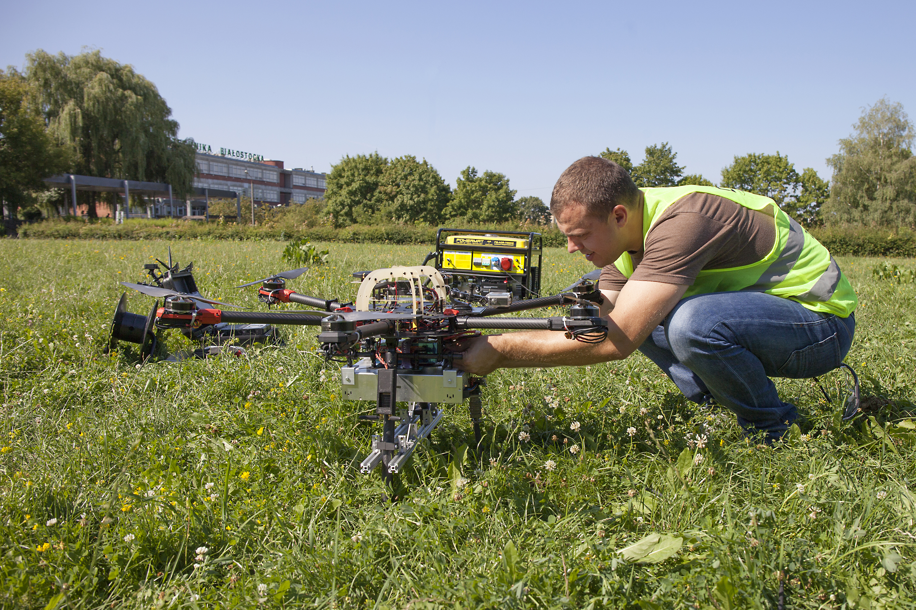 Tests of AVAL system components carried out at the Białystok University of Technology. In the photo, a man in a yellow protective vest is working on a drone in a meadow
