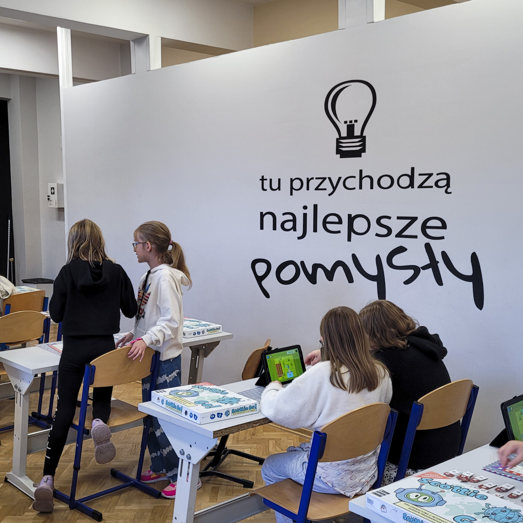 Uczestnicy CODEWEEK 2024 na tle ścianki z hasłem: Tu przychodzą najlepsze pomysły.