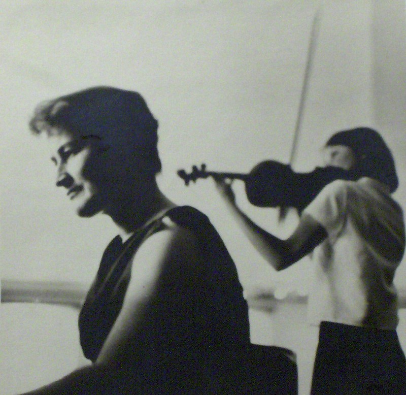 Czarno-białe zdjęcie z koncertu. Na pierwszym planie M. Andrzejewska przy fortepianie. Za nią stoi A Strzałkowska i gra na skrzypcach.