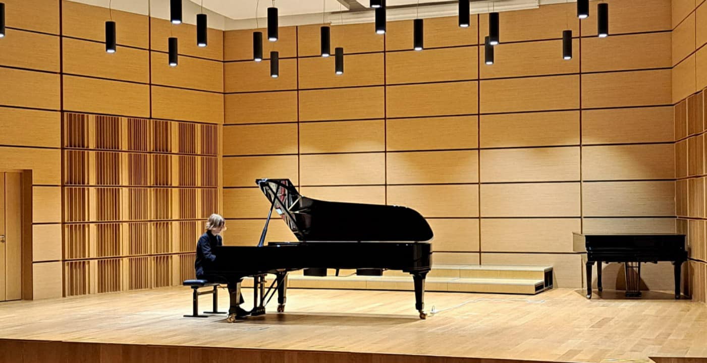 Pianista ubrany na czarno grający na fortepianie na sali koncertowej.