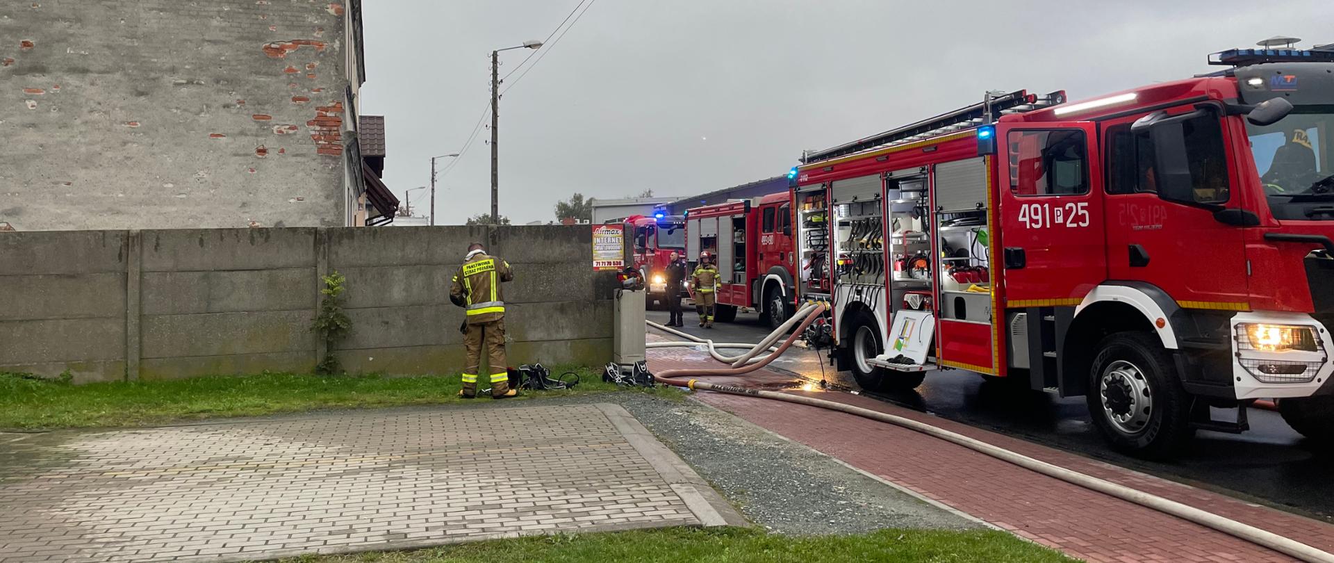 Zdjęcie przedstawia teren działań na tle pojazdów pożarniczych 