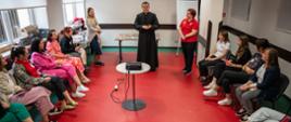 Participants of the training session listening to two women and a priest standing next to a desk with teaching materials