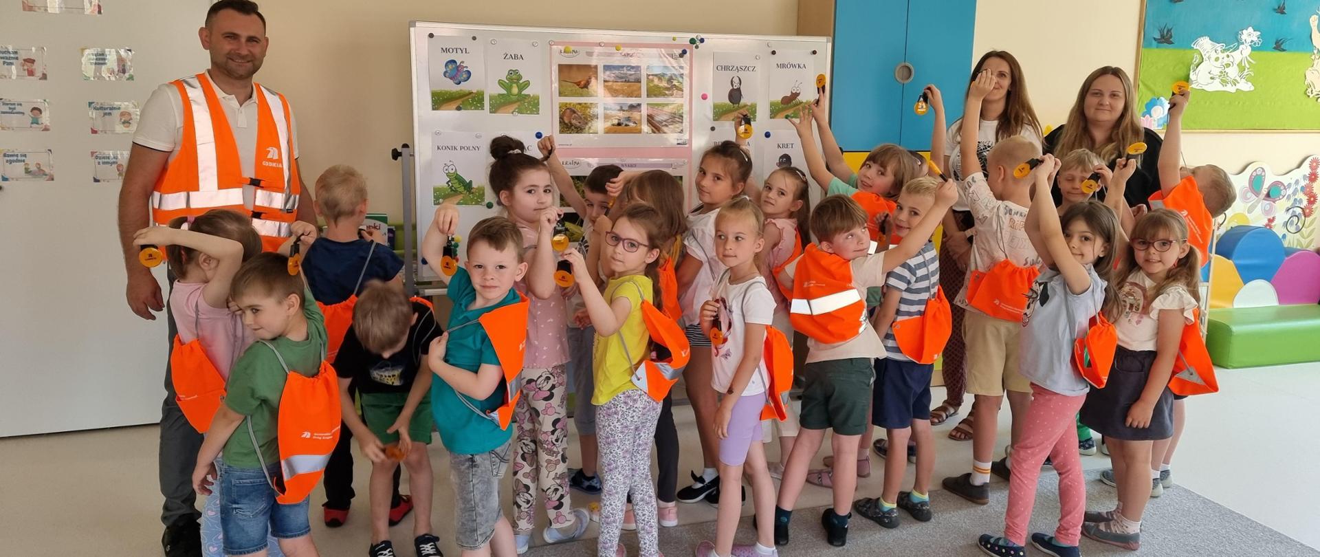 Lekcja bezpieczeństwa - grupa dzieci z odblaskowymi pomarańczowymi plecakami 