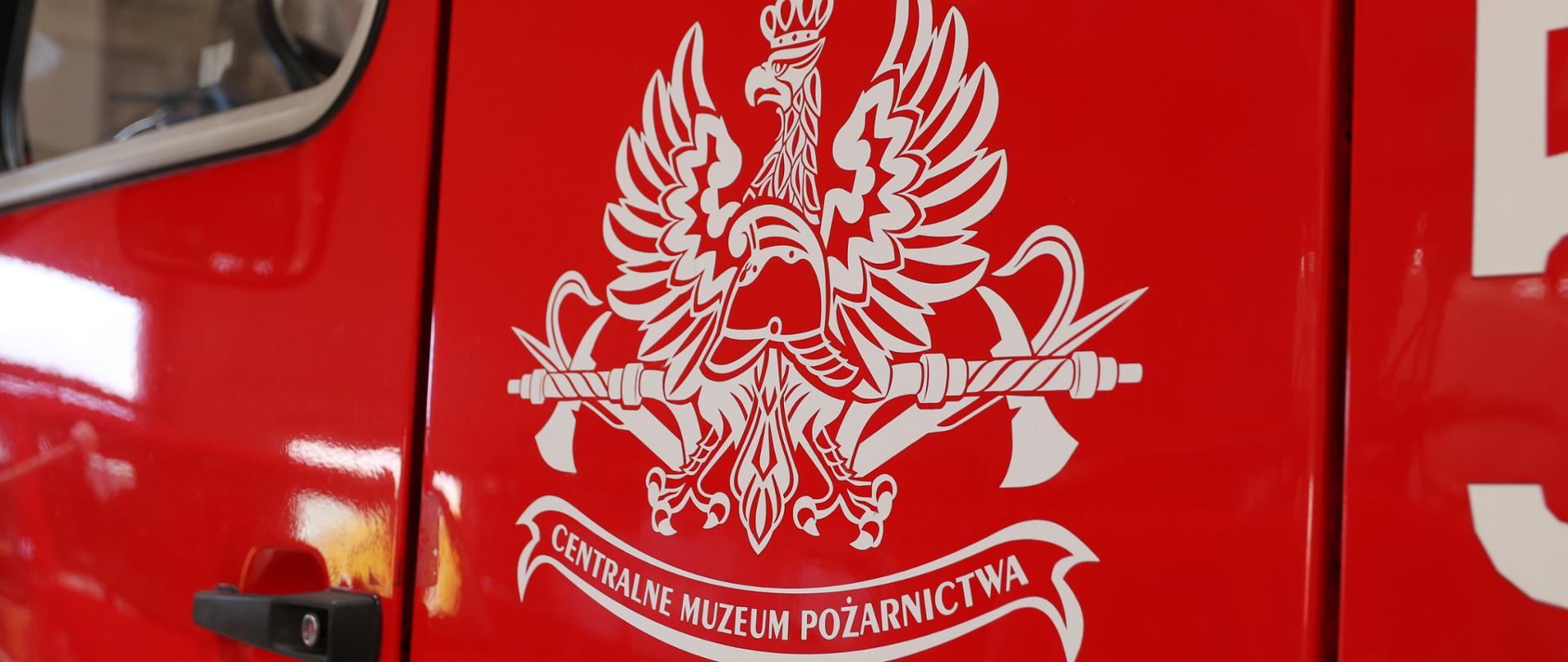 Drzwi czerwonego samochodu, a na nich białe logo Centralnego Muzeum Pożarnictwa