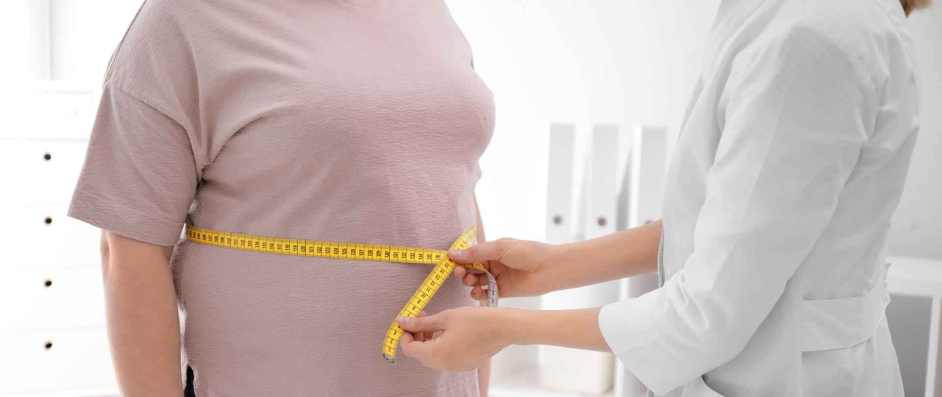 Doctor measuring waist of overweight woman in clinic, closeup