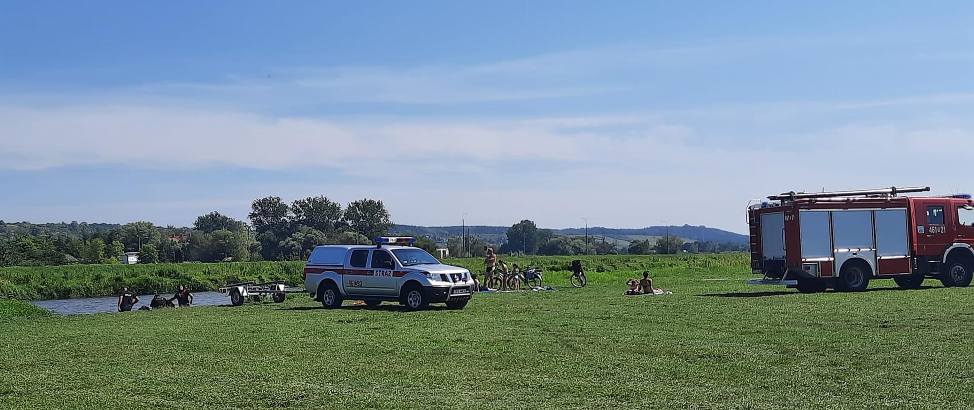 Zdjęcie przedstawia strażaków wodujących ponton na brzegu rzeki. W tle widać wóz pożarniczy.