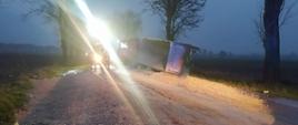 Na zdjęciu droga wojewódzka zablokowana przez leżące na niej kruszywo i uszkodzony samochód ciężarowy z naczepą, wzdłuż drogi rosną drzewa 