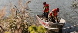 Na zdjęciu widocznych jest dwóch strażaków znajdujących się w łódce na akwenie wodnym.