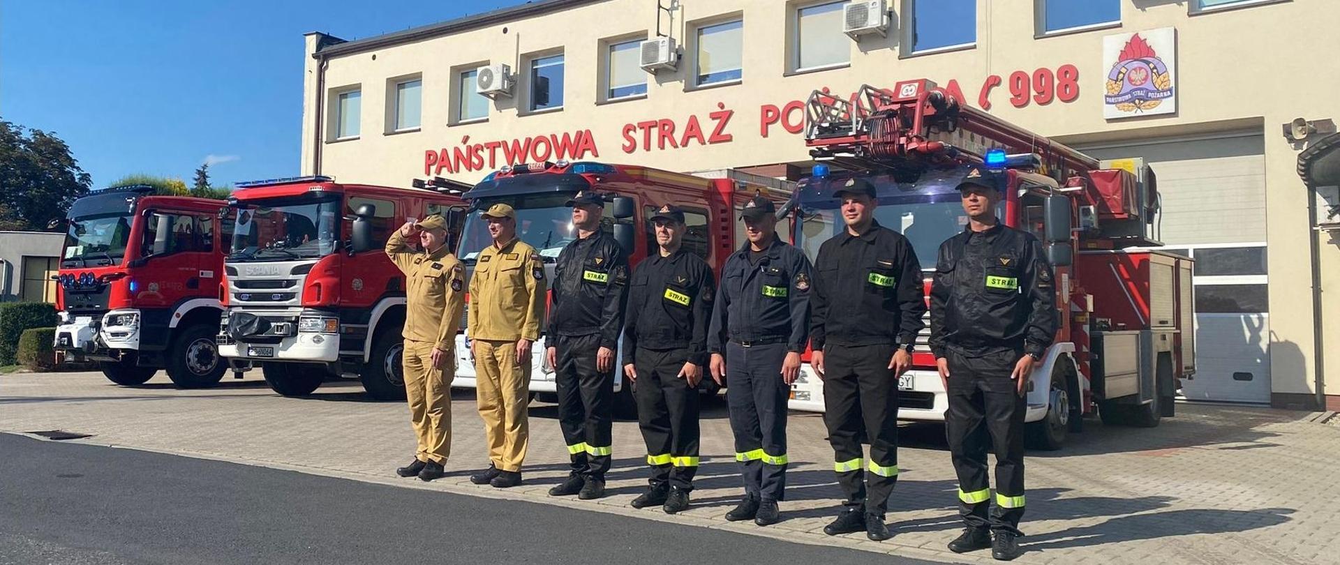 Zmiana Służbowa podczas oddawania hołdu z okazji 80. rocznicy wybuchu Powstania Warszawskiego. Strażacy na tle samochodów pożarniczych z włączonymi sygnałami świetlnymi i dźwiękowymi.