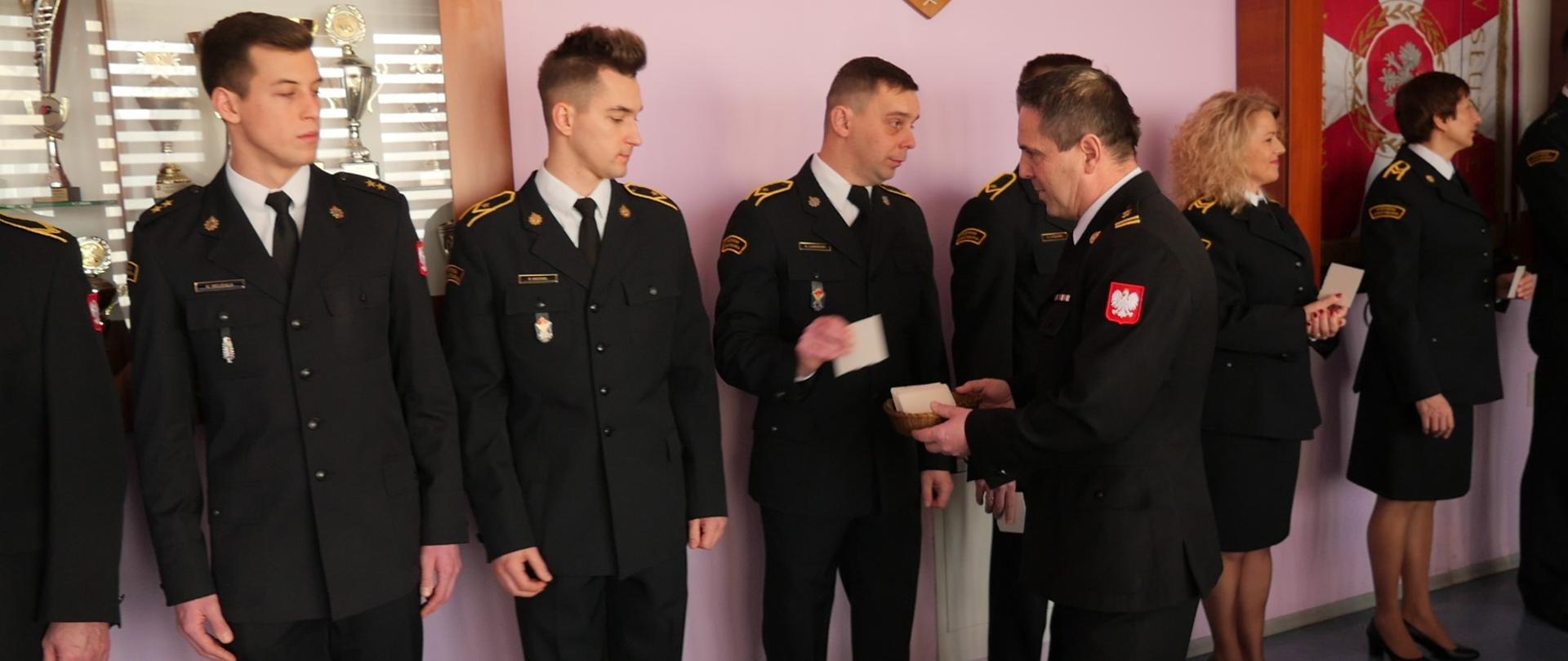 Strażacka Wigilia, zastępca komendanta rozdaje opłatki ustawionym w szeregu strażakom, wszyscy u mundurach wyjściowych