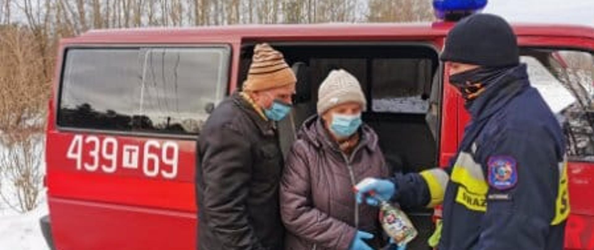 Strażak OSP Ruda Maleniecka pomaga wysiąść starszej kobiecie i starszemu mężczyźnie z samochodu strażackiego.
