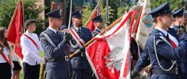 Policjanci trzymają sztandar oraz szable. Ubrani są w mundury. W tle widać również uczniów szkoły. 