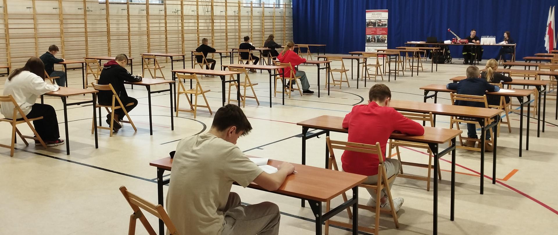 Na zdjęciu widać dzieci ze szkół podstawowych siedzących w ławkach szkolnych, piszących test konkursu Ogólnopolskiego Turnieju Wiedzy Pożarniczej.