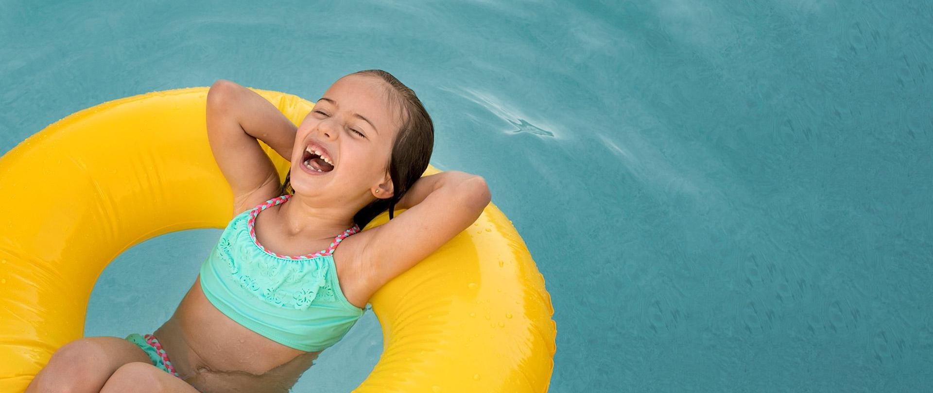 Roześmiana dziewczynka pływa w dmuchanym kole w basenie.