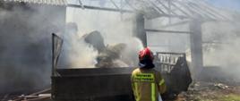 Na zdjęciu strażak podaje prąd wody na palący się obiekt stodoły.