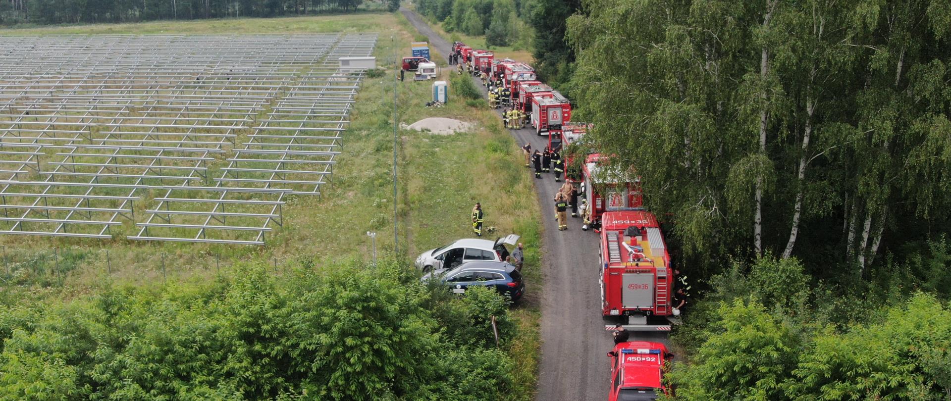 Pojazdy gaśnicze strażaków stoją ustawione w gotowości do działań.