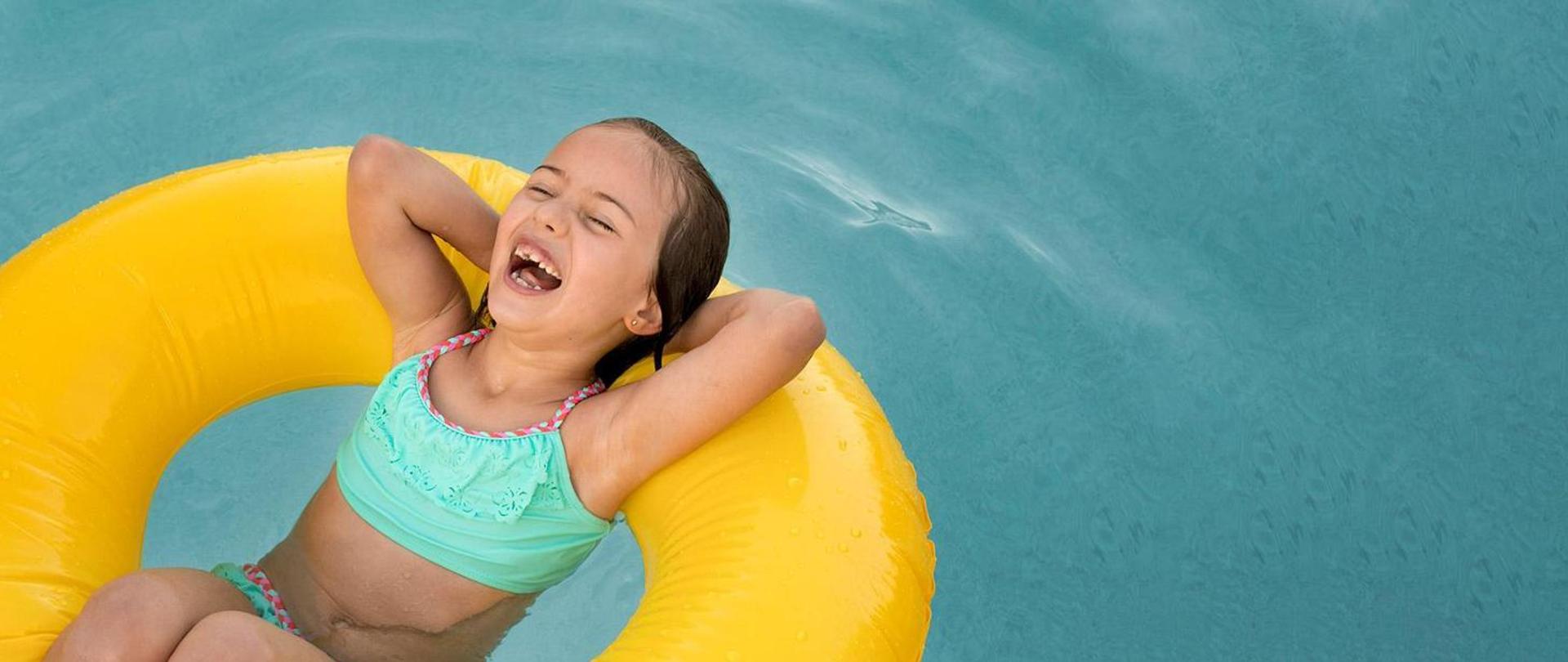 Roześmiana dziewczynka pływa w dmuchanym kole w basenie