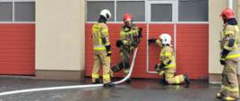 Zdjęcie przedstawia strażaków podczas ćwiczenia wejścia do pomieszczenia, w którym rozwija się pożar pod okiem instruktorów.