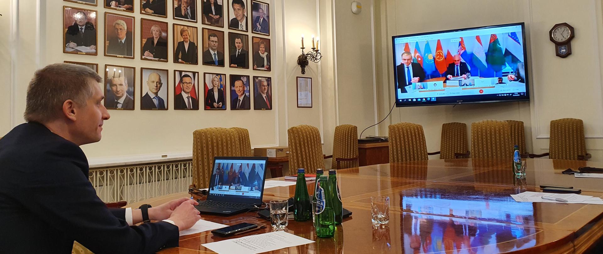 wiceminister Piotr Nowak podczas spotkania Gubernatorów MFW i Banku Światowego, przed nim telebim, na którym widać innych uczestników, na ścianie wiszą portrety polskich ministrów finansów