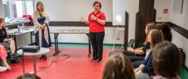 Participants of the training session listening to two women standing next to a desk with teaching materials 