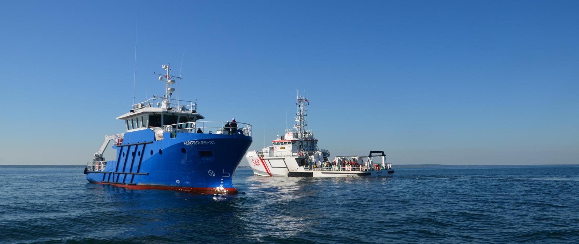 niebieski statek inspekcyjny mijający biały statek na spokojnym i błękitnym morzu