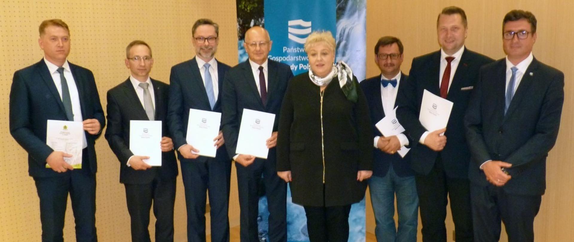 Uczestnicy konferencji w sprawie Zalewu Zemborzyckiego pozują wspólnie do zdjęcia. W dłoniach mają białe teczki.