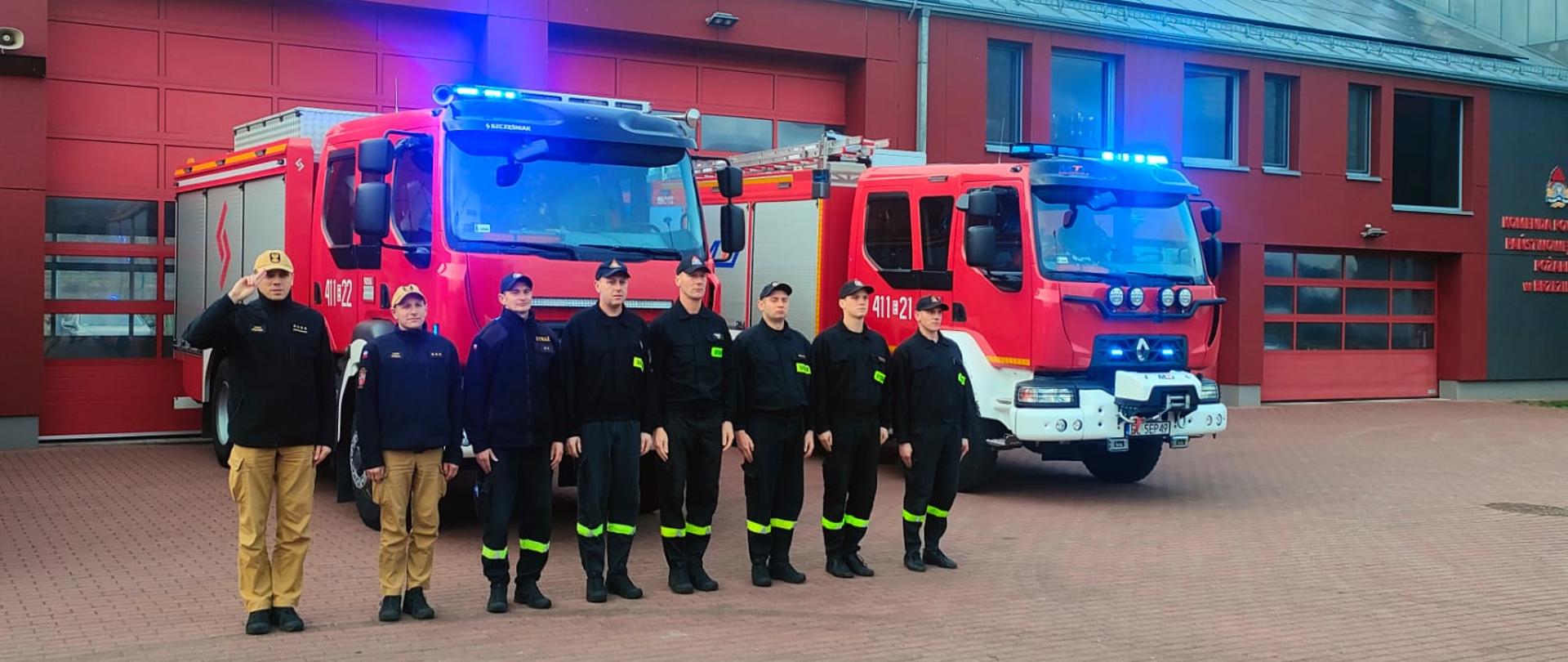 Hołd dla zmarłego ratownika medycznego, zmiana służbowa oddaje hołd zmarłemu ratownikowi medycznemu, stoi przed samochodami gaśniczymi , które zostały wyprowadzone przed budynek komendy, samochody mają włączone sygnały świetlne i dźwiękowe, dowódca oddaje honor salutując.