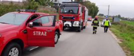 Zdjęcie przedstawia samochody pożarnicze oraz radiowóz obecne na miejscu zdarzenia. Obok pojazdów widać strażaka PSP w umundurowaniu bojowym oraz policjanta. 