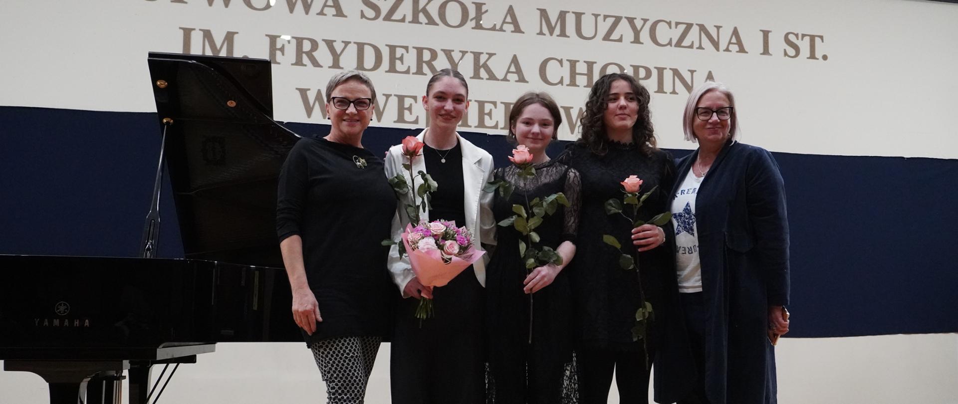 Na sali koncertowej pozują do zdjęcia absolwentki Emilia Sanecka, Agata Sulborska, Zofia Pałasz oraz nauczycielki Elżbieta Lieder i Beata Felczykowska