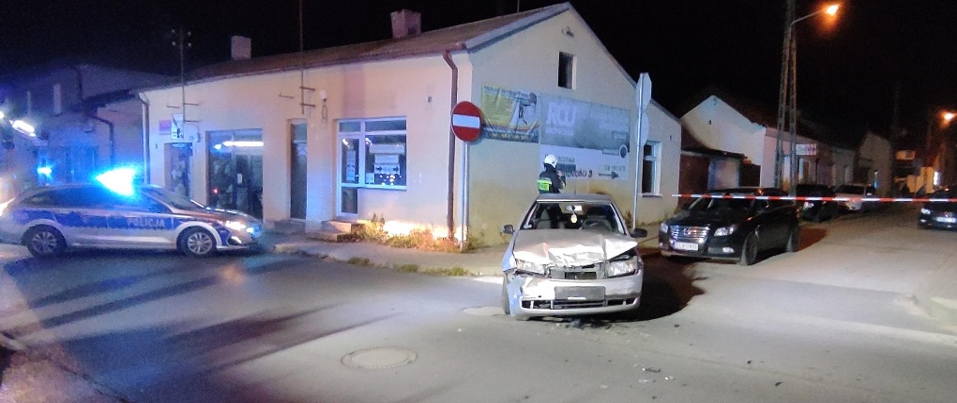 Skrzyżowanie ulic Kilińskiego i Kościuszki, pora nocna na pierwszym planie rozbity samochód osobowy, na drugim planie zabezpieczenie miejsca akcji poprzez radiowóz Policji oraz biało–czerwoną taśmę.