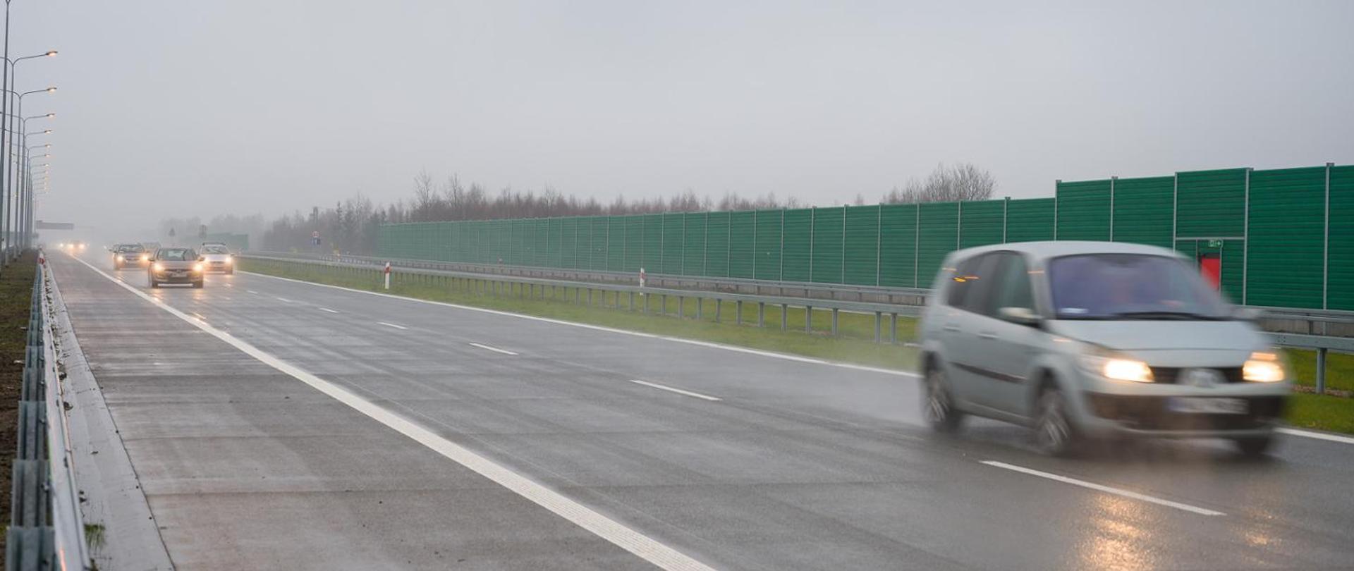 Samochody jadące dwujezdniową drogą ekspresową z włączonymi światłami - mglisto, deszczowo, mokra jezdnia