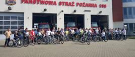Nr 3 Uczestnicy rajdu rowerowego stoją trzymając swoje rowery. W tle budynek KP PSP w Kazimierzy Wielkiej