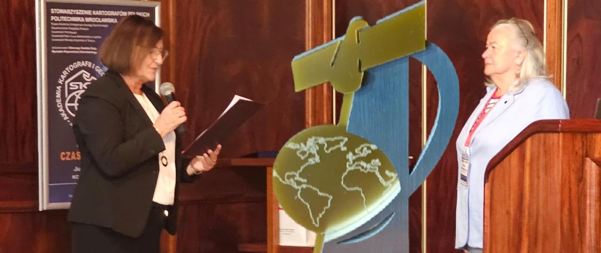 Zdjęcie przedstawia Głównego Geodetę Kraju Alicję Kulkę i Przewodniczącą Zarządu Głównego SKP dr hab. inż. Joannę Bac-Bronowicz podczas IV Akademii Kartografii i Geoinformatyki Modelowanie czasoprzestrzenne