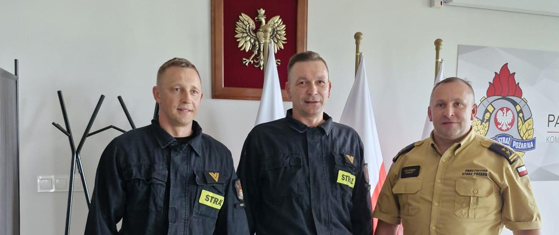 Nagrodzeni Funkcjonariusze (od lewej) st. ogn. Mirosław Rost oraz st.ogn. Krzysztof Żaczek oraz Komendant Powiatowy PSP w Pucku uśmiechają się do autora zdjęcia. Funkcjonariusze trzymają w rękach nagrody jubileuszowe wręczone przez Komendanta.