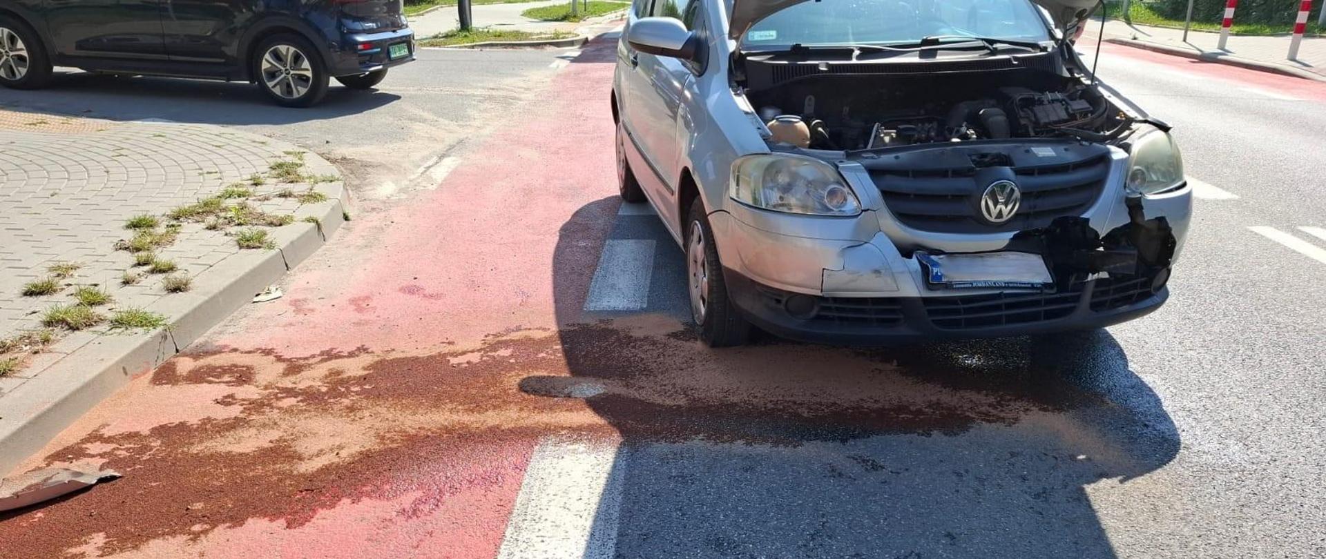 Zdjęcie przedstawia ulicę Wojska Polskiego gdzie doszło do wypadku: na pierwszym planie stoi uszkodzony samochód osobowy , pod którym widać plamę sorbentu wchłaniającego rozlane płyny.