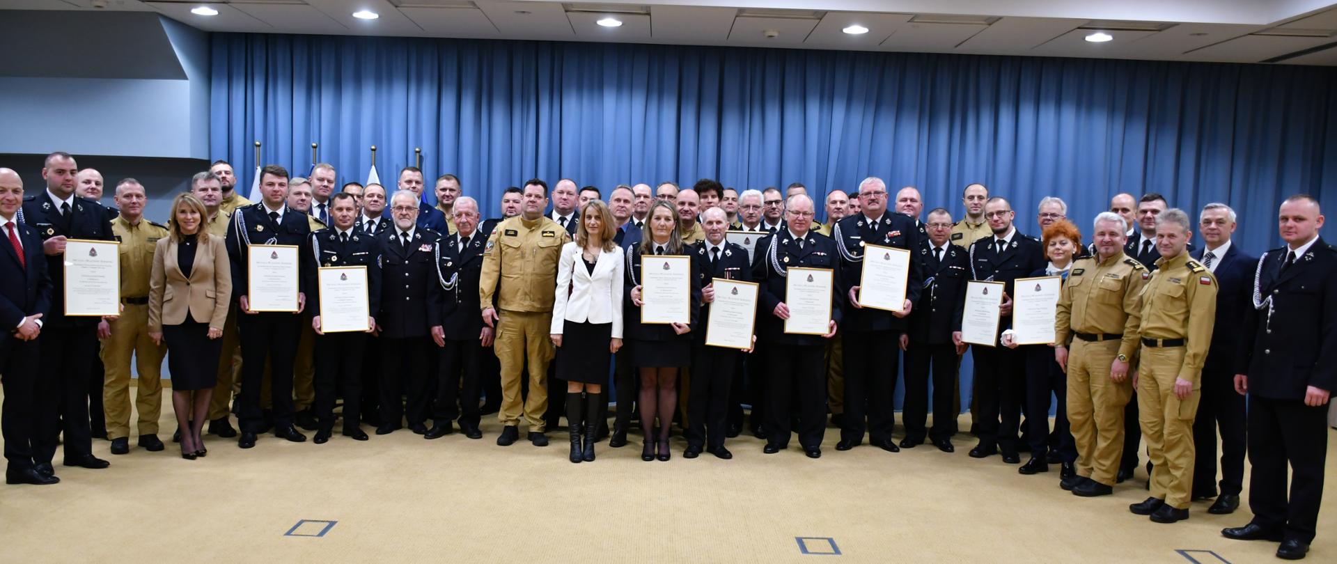 Zdjęcie grupowe uczestników uroczystości. Strażacy OSP trzymają wręczone decyzje oprawione w ramki. 