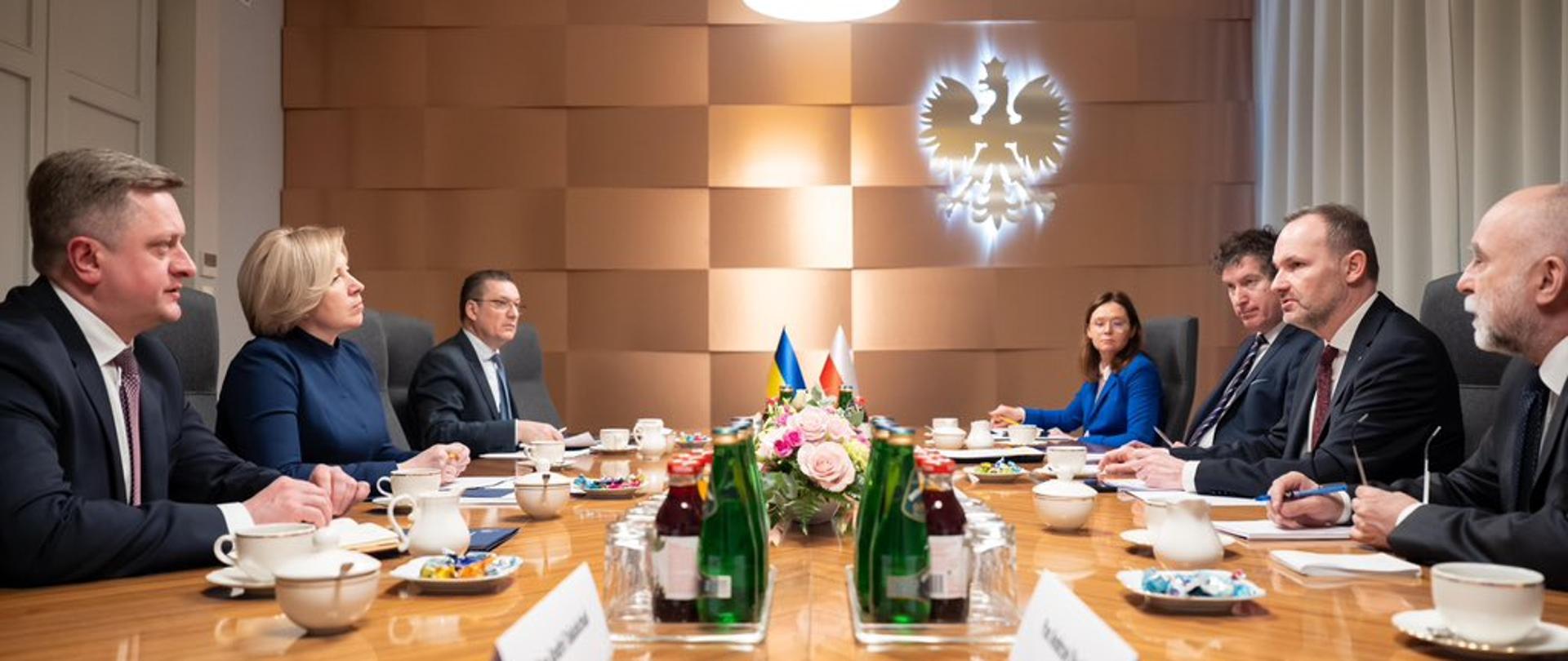 Na zdjęciu widać uczestników polsko-ukraińskich konsultacji międzyrządowych. Uczestnicy siedzą przy stole i rozmawiają. Po prawej stronie widać reprezentację strony polskiej, w tym ministra Krzysztofa Hetmana. Po lewej stronie reprezentacja strony ukraińskiej. 