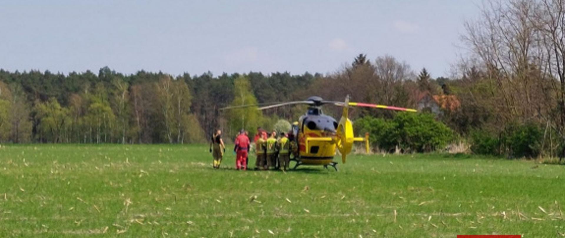 Helikopter stoi na polu obok stoją strażacy i ratownicy.