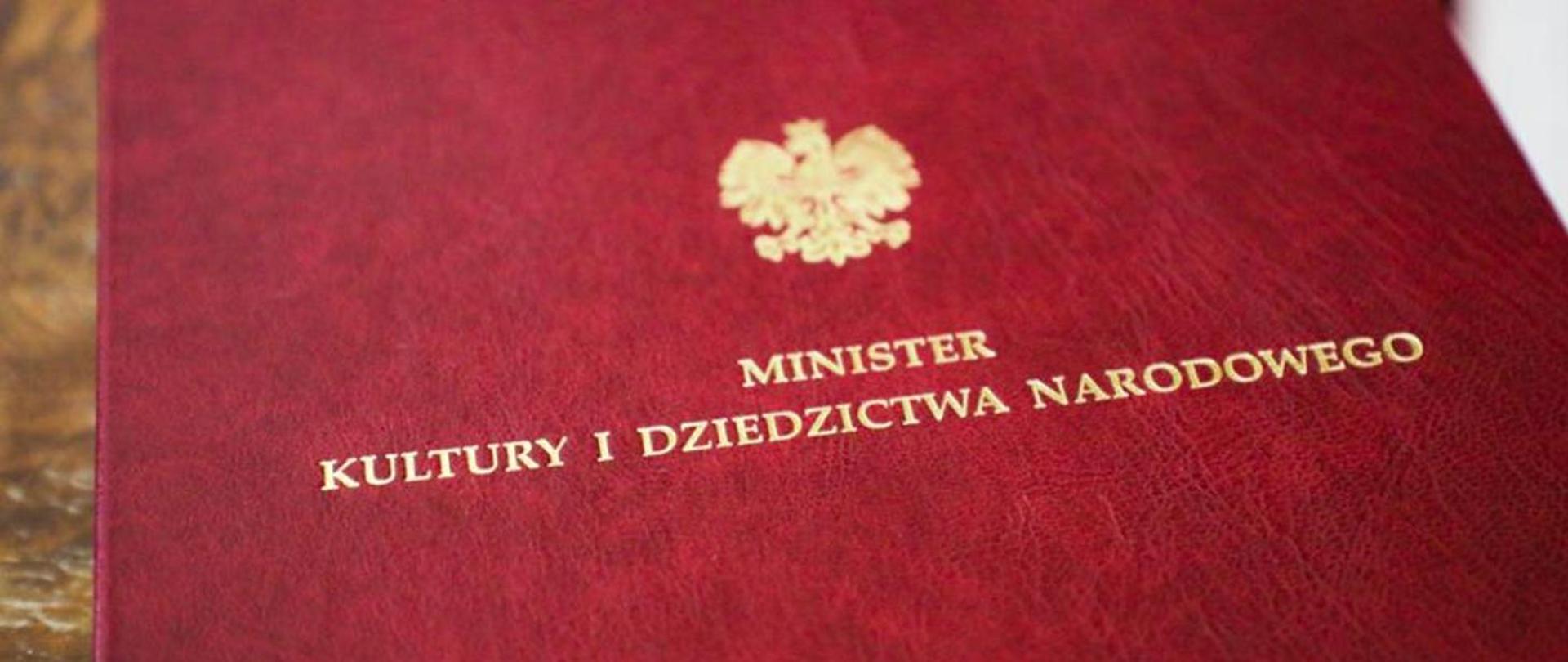 Zdjęcie . Czerwona teczka z napisem Minister Kultury i Dziedzictwa Narodowego. Nad napisem symbol orła w koronie.