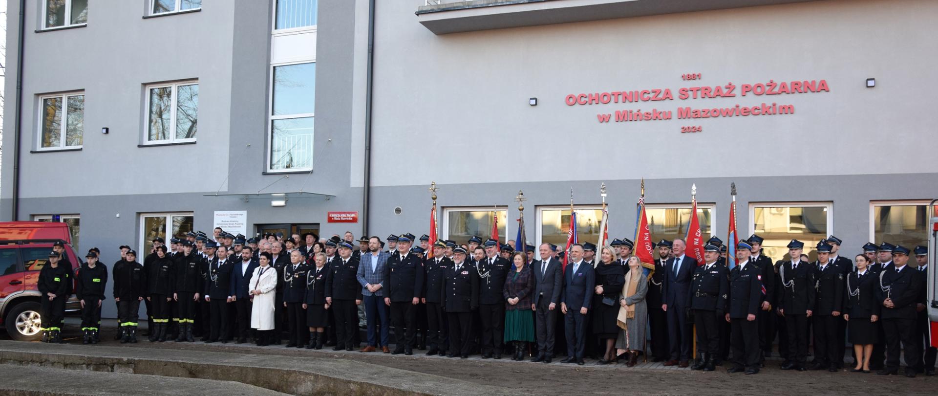 Zdjęcie grupowe uczestników uroczystości na tle nowej strażnicy OSP w Mińsku Mazowieckim. 