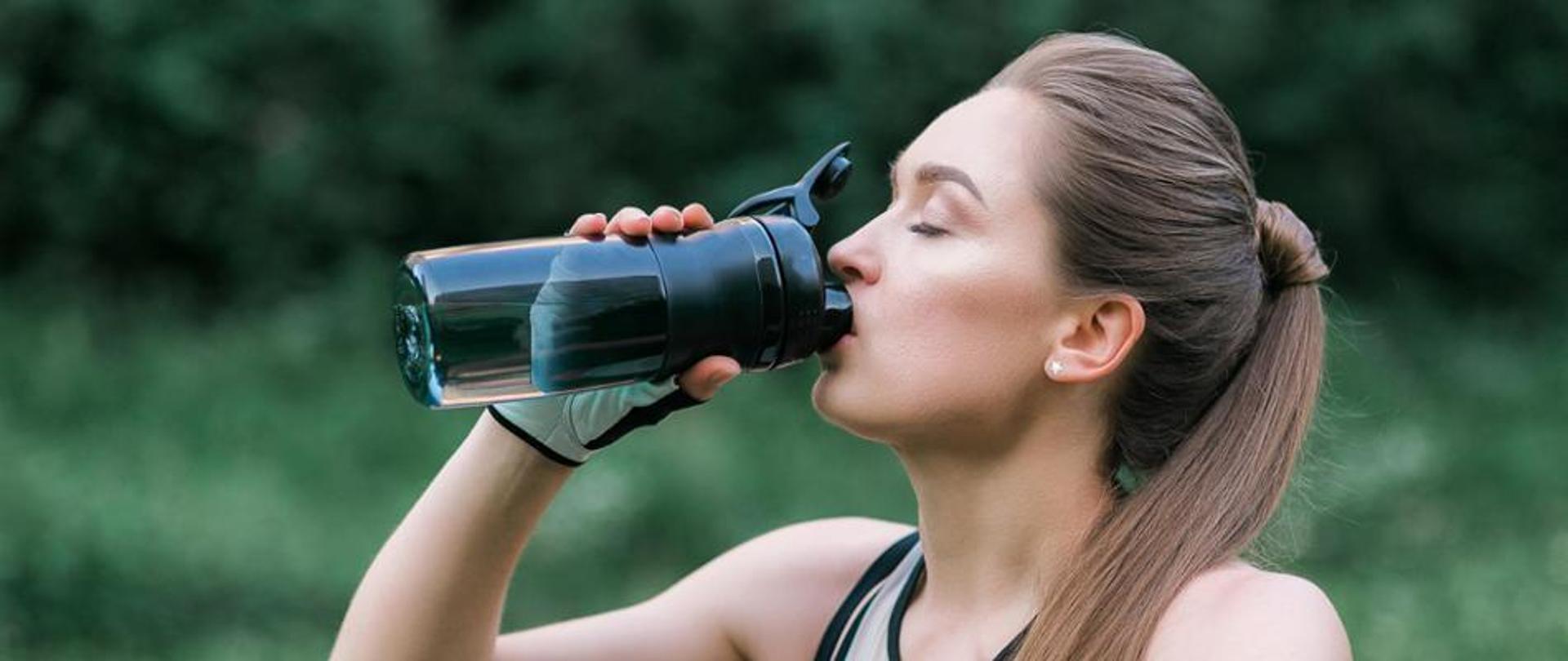 kobieta pijąca napój z ciemnego bidonu 